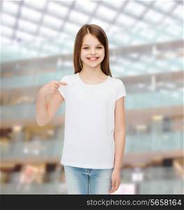 advertising, childhood, gesture and people - smiling girl in white t-shirt pointing finger on herself over shopping center background