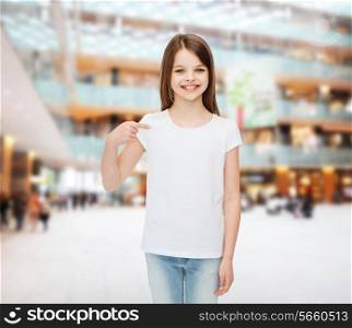 advertising, childhood, gesture and people - smiling girl in white t-shirt pointing finger on herself over shopping center background