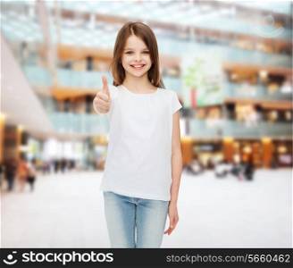 advertising, childhood, gesture, consumerism and people - smiling girl in white t-shirt showing thumbs up over shopping center background
