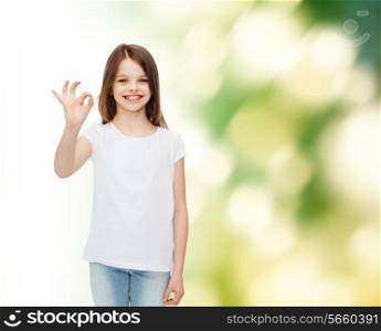 advertising, childhood, gesture, ecology and people - smiling little girl in white blank t-shirt showing ok sign over green background