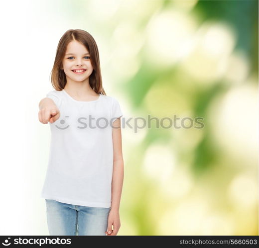 advertising, childhood, gesture, ecology and people - smiling little girl in white blank t-shirt pointing finger on you over green background