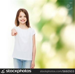 advertising, childhood, gesture, ecology and people - smiling little girl in white blank t-shirt pointing finger on you over green background