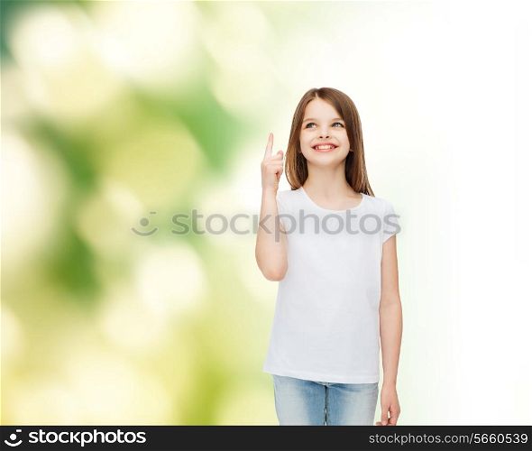advertising, childhood, gesture, ecology and people - smiling little girl in white t-shirt pointing her finger up over green background