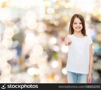 advertising, childhood, gesture, holidays and people - smiling little girl in white t-shirt pointing finger on you over sparkling background