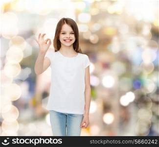 advertising, childhood, gesture, holidays and people - smiling little girl in white blank t-shirt showing ok sign over sparkling background