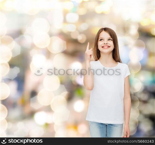 advertising, childhood, gesture, holidays and people - smiling little girl in white blank t-shirt pointing her finger up over sparkling background