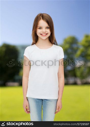 advertising, childhood, nature and people - smiling little girl in white blank t-shirt over green park background