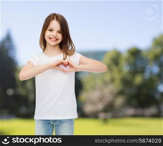 advertising, childhood, nature, charity and people - smiling girl in white t-shirt making heart-shape gesture over green park background