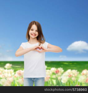 advertising, childhood, nature, gesture and people concept - smiling girl in white t-shirt making heart-shape gesture over field background