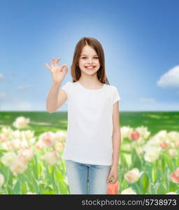 advertising, childhood, nature, gesture and people concept - smiling girl in white t-shirt showing ok sign over flower field background