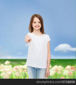 advertising, childhood, nature, gesture and people concept - smiling little girl in white blank t-shirt pointing finger on you over flower field background