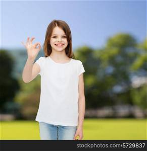 advertising, childhood, nature, gesture and people - smiling little girl in white blank t-shirt showing ok sign over green park background