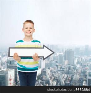 advertising, direction and childhood concept - smiling little boy with white blank arrow pointing up over city background