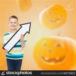 advertising, direction, holidays and people - smiling little boy holding big white arrow over halloween pumpkins background