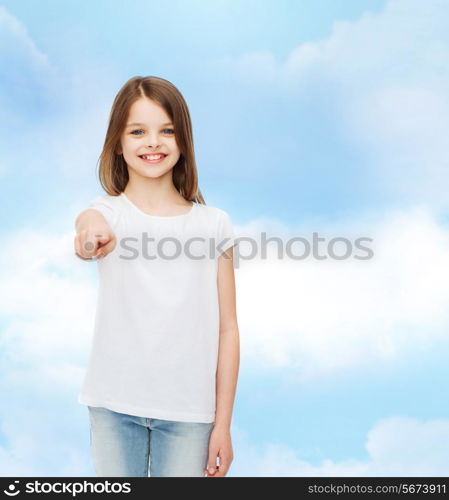 advertising, dream, childhood, gesture and people - smiling little girl in white t-shirt pointing finger on you over cloudy sky background