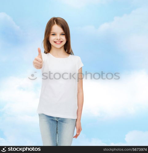 advertising, dream, childhood, gesture and people - smiling little girl in white blank t-shirt showing thumbs up over cloudy sky background