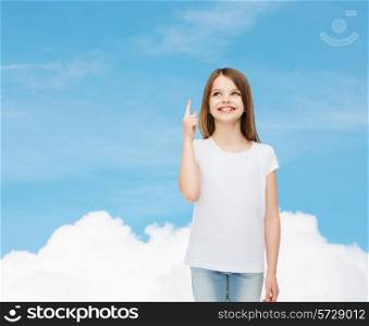 advertising, dream, childhood, gesture and people - smiling little girl in white blank t-shirt pointing finger up over blue sky background