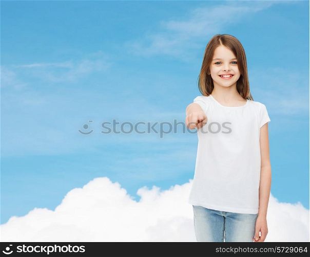 advertising, dream, childhood, gesture and people - smiling little girl in white t-shirt pointing finger on you over blue sky background