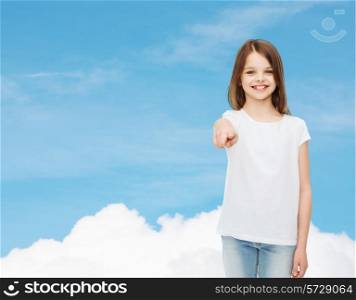 advertising, dream, childhood, gesture and people - smiling little girl in white t-shirt pointing finger on you over blue sky background
