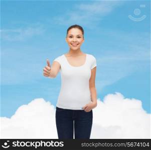 advertising, dream, gesture and people concept - smiling young woman in blank white t-shirt showing thumbs up over blue sky background
