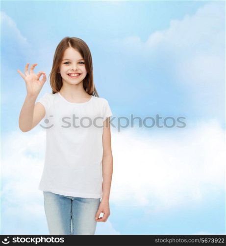 advertising, dream, gesture, childhood and people - smiling little girl in white blank t-shirt showing ok sign over cloudy sky background
