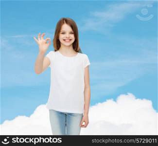 advertising, dream, gesture, childhood and people - smiling little girl in white blank t-shirt showing ok sign over blue sky background