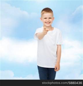advertising, dream, people and childhood concept - smiling boy in white blank t-shirt pointing finger at you over cloudy sky background