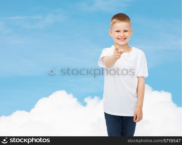 advertising, dream, people and childhood concept - smiling little boy in white blank t-shirt pointing finger at you over sky background