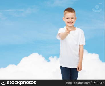 advertising, dream, people and childhood concept - smiling little boy in white blank t-shirt pointing finger at you over sky background