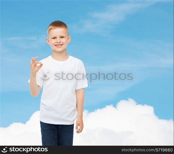 advertising, dream, people and childhood concept - smiling little boy in white blank t-shirt making ok gesture over sky background