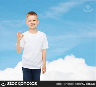 advertising, dream, people and childhood concept - smiling little boy in white blank t-shirt making ok gesture over sky background