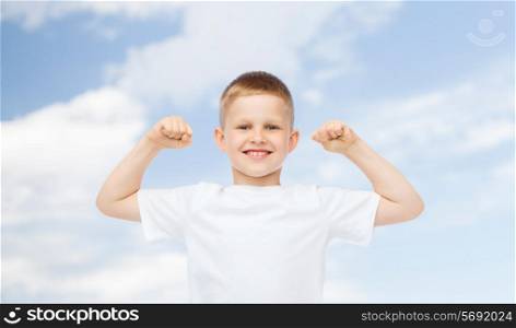 advertising, ecology, people and childhood concept - smiling little boy in white blank t-shirt flexing biceps over blue sky background