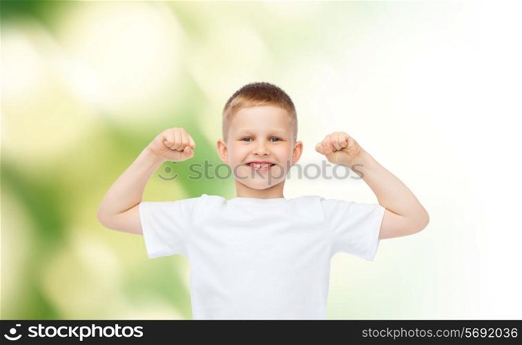 advertising, ecology, people and childhood concept - smiling little boy in white blank t-shirt flexing biceps over green background