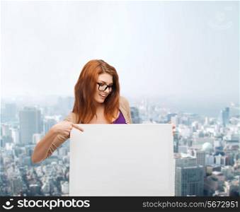 advertising, education and people concept - smiling teenage girl in glasses pointing finger to blank white board over city background