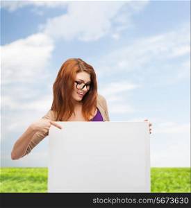 advertising, education and people concept - smiling teenage girl in glasses pointing finger to blank white board over blue sky and grass background