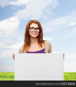 advertising, education and people concept - smiling teenage girl in glasses with blank white board over blue sky and grass background