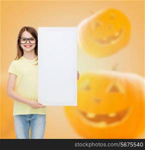 advertising, education, holidays and people concept - smiling little girl in glasses with white board over halloween pumpkins background