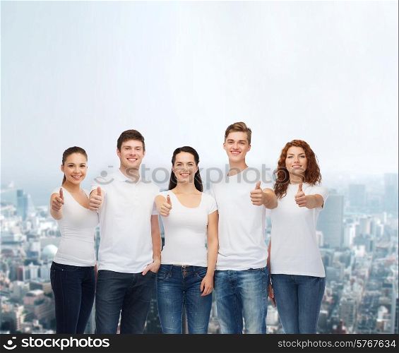 advertising, friendship, and people concept - group of smiling teenagers in white blank t-shirts showing thumbs up over city background