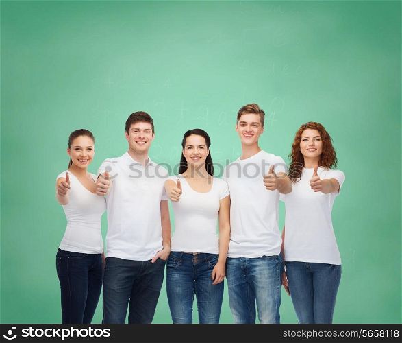 advertising, friendship, education, school and people concept - group of smiling teenagers in white blank t-shirts showing thumbs up over green board background