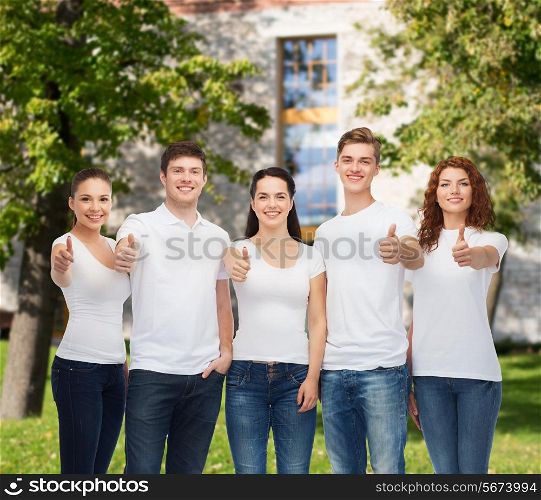 advertising, friendship, education, school and people concept - group of smiling teenagers in white blank t-shirts showing thumbs up over campus background