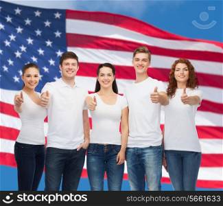 advertising, friendship, patriotism and people concept - group of smiling teenagers in white blank t-shirts showing thumbs up over american flag background