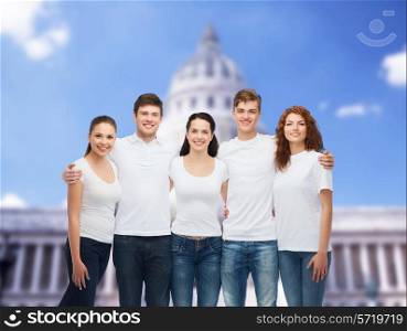 advertising, friendship, tourism and people concept - group of smiling teenagers in white blank t-shirts over white house background