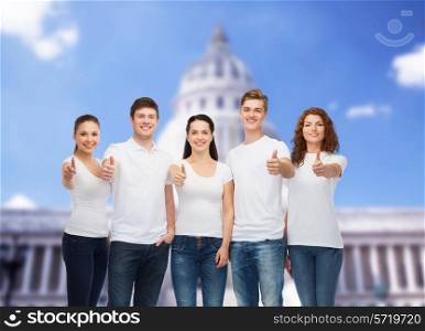 advertising, friendship, tourism and people concept - group of smiling teenagers in white blank t-shirts showing thumbs up over over white house background