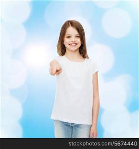 advertising, gesture, childhood and people - smiling little girl in white blank t-shirt pointing finger at you over blue background