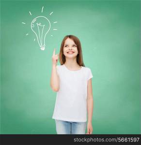 advertising, gesture, education, childhood and people - smiling little girl in white t-shirt pointing finger up over green board with doodle background