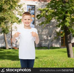 advertising, gesture, people and childhood concept - smiling boy in white blank t-shirt pointing fingers at himself over campus background