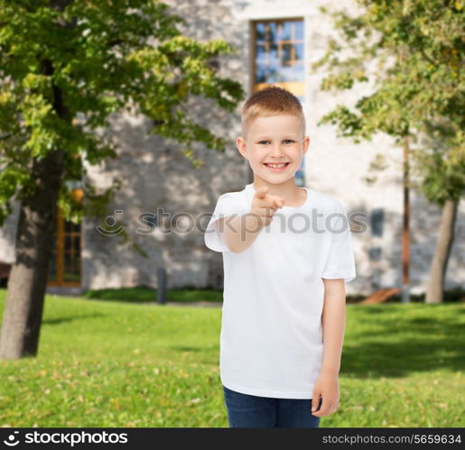 advertising, gesture, people and childhood concept - smiling little boy in white blank t-shirt pointing finger at you over campus background
