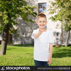 advertising, gesture, people and childhood concept - smiling little boy in white blank t-shirt pointing finger at you over campus background