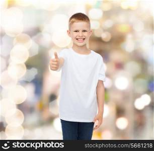 advertising, gesture, people and childhood concept - smiling little boy in white blank t-shirt showing thumbs up over holidays background