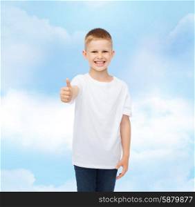 advertising, gesture, people and childhood concept - smiling little boy in white blank t-shirt showing thumbs up over cloudy sky background